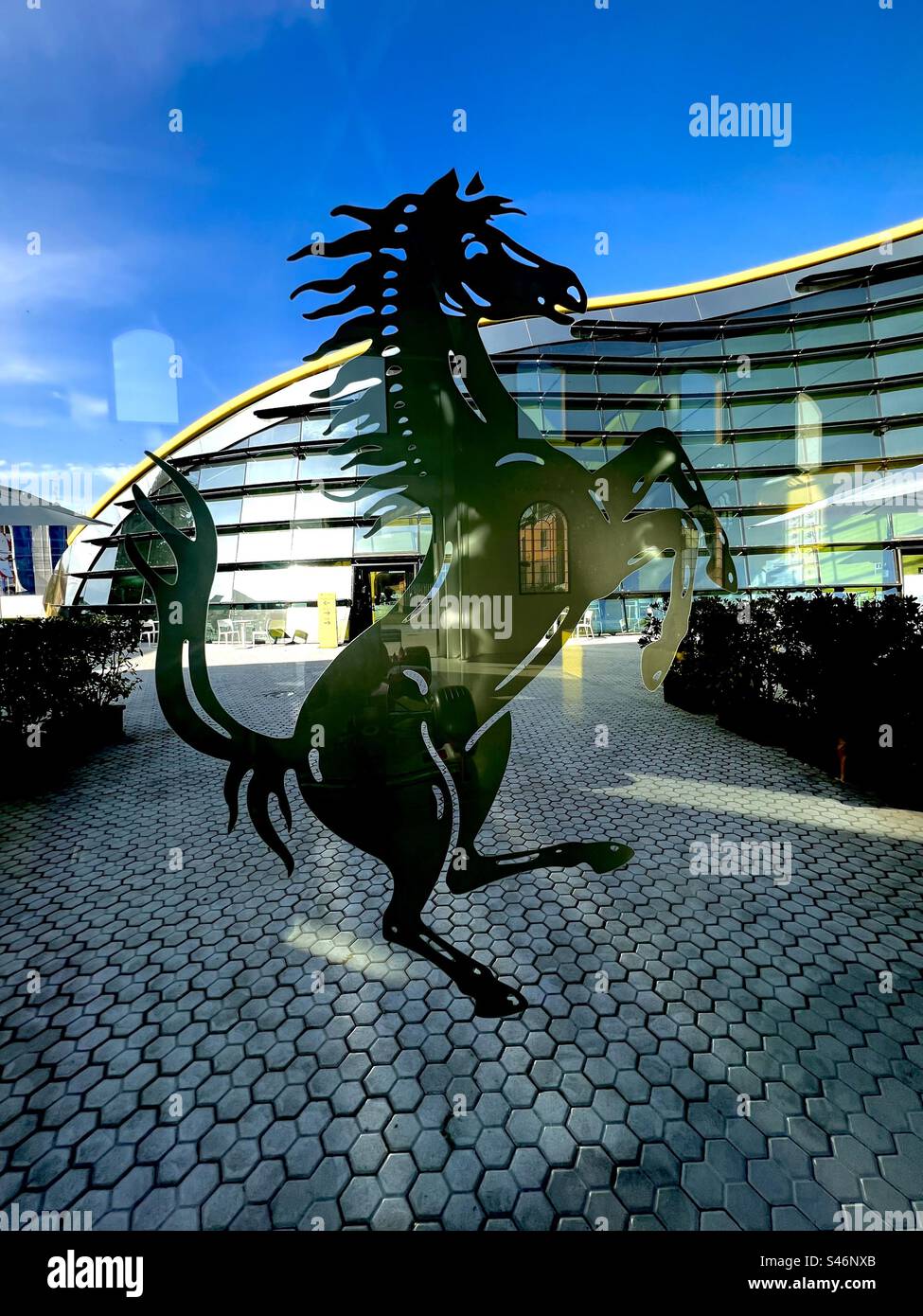 Prancing horse symbol in window of the museum of Enzo Ferrari’s birthplace, looking out to the newer glass building of Museo Enzo Ferrari in Modena - Smartphone Captured Stock Image