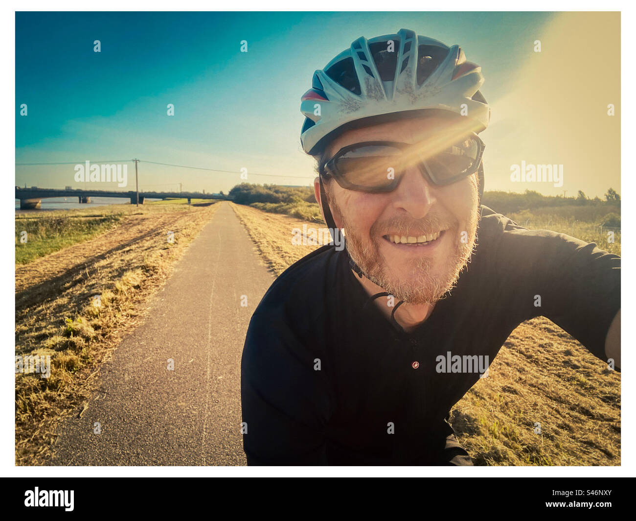 A happy cyclist rides in the sun along a flat cycling lane near Kings Lynn in Norfolk Stock Photo