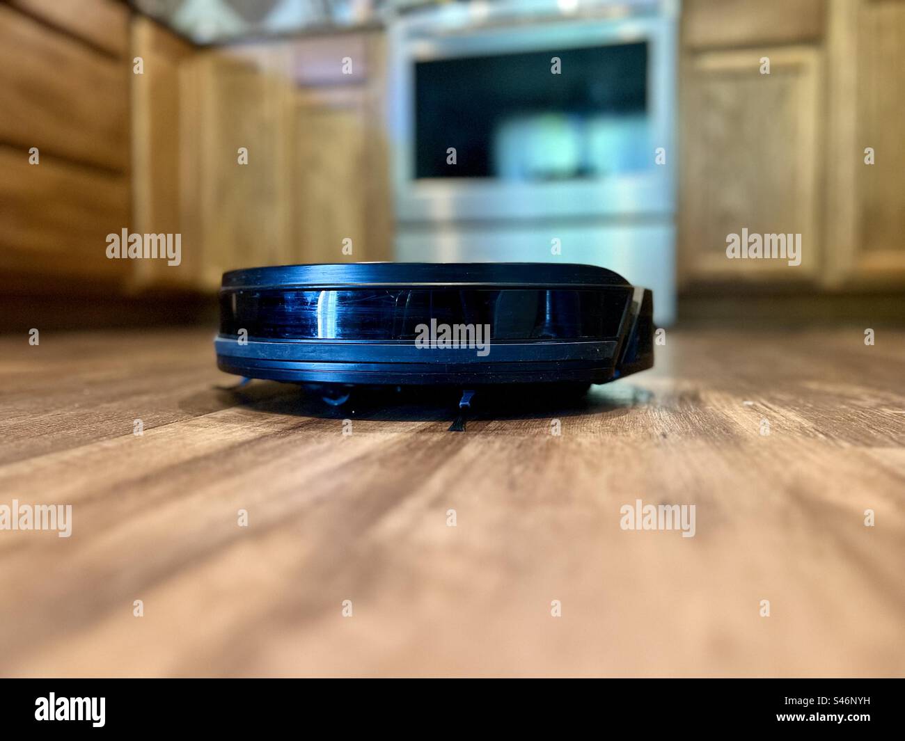 Robotic vacuum cleaner cleaning a kitchen floor - Smartphone Captured Stock Image