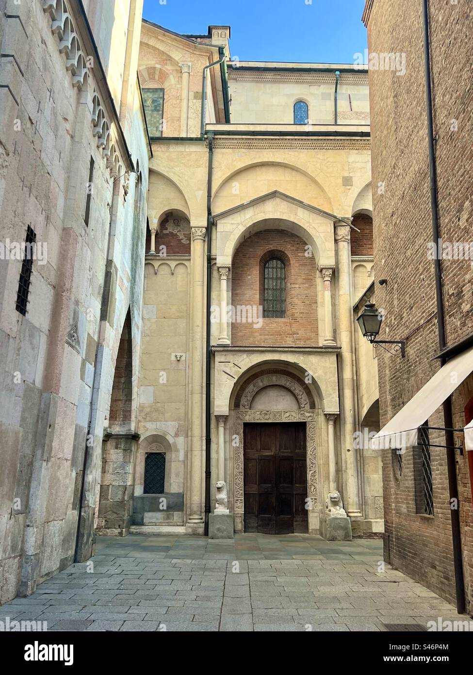 A small cobblestone alley near the Museu di Duomo in Modena. On the left is the bell tower structure that tilts to the street and is also known as the leaning tower of Modena - Smartphone Captured Stock Image