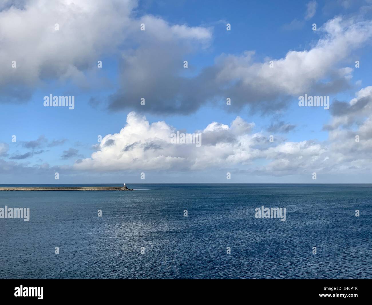 Blue seascape scene with lighthouse on harbour peninsular, Fishguard, Pembrokeshire, Wales - Smartphone Captured Stock Image