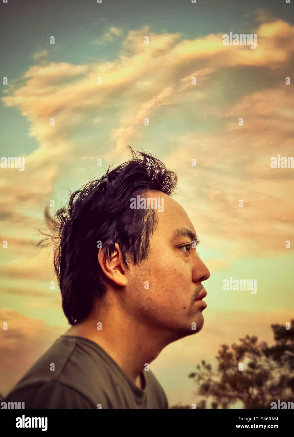 Portrait of young Asian man lost in contemplation against pink clouds in blue sunset sky. Wind. Blowing. Windswept. Motion. - Smartphone Captured Stock Image Portrait of young Asian man lost in contemplation against pink clouds in blue sunset sky. Wind. Blowing. Windswept. Motion. - Smartphone Captured Stock Image