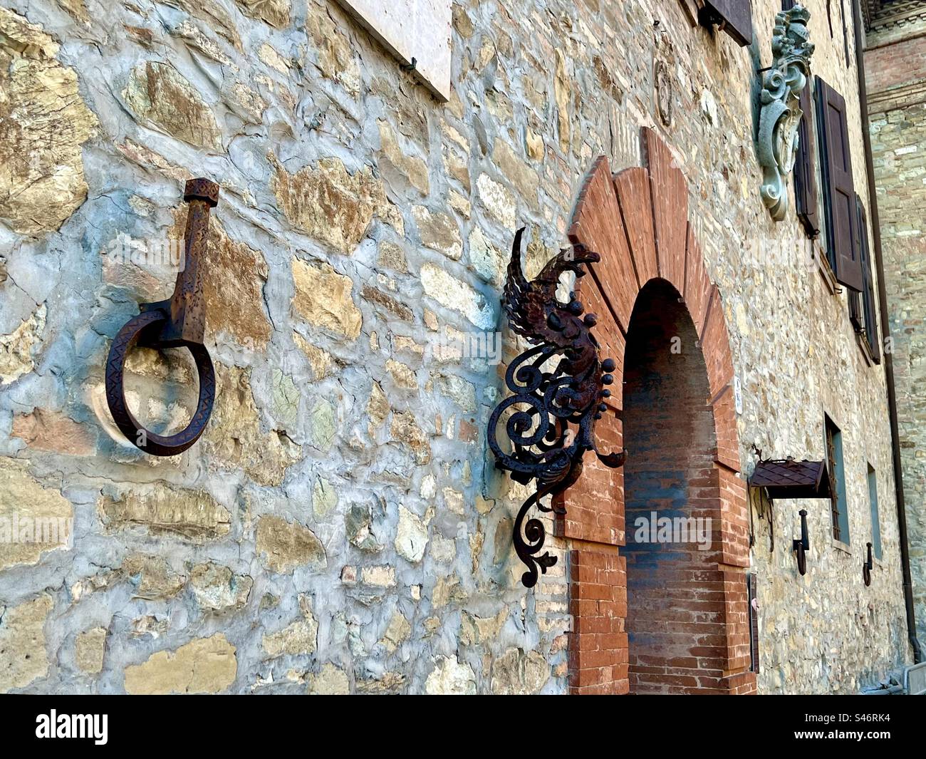 Bricks lining an arch doorway and wrought iron decorations on the exterior of building at Castello di Montegibbio - Smartphone Captured Stock Image