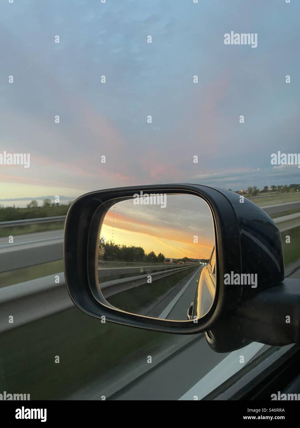 The car's left mirror captures the serene beauty of a sunset, reflecting the mesmerizing hues of the fading day. - Smartphone Captured Stock Image