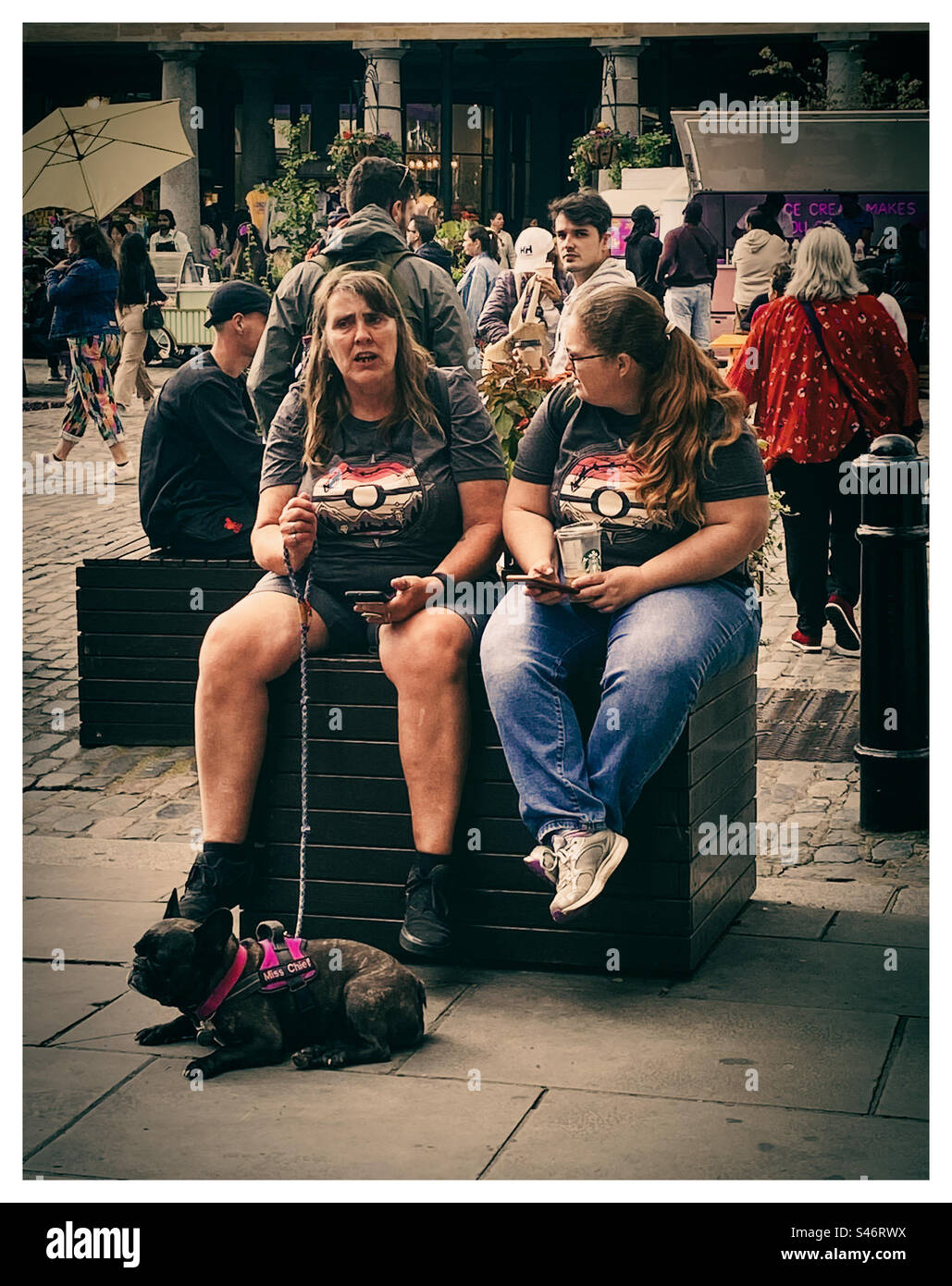 Two women in matching t shirts with a french bulldog in Covent Garden London England UK - Smartphone Captured Stock Image