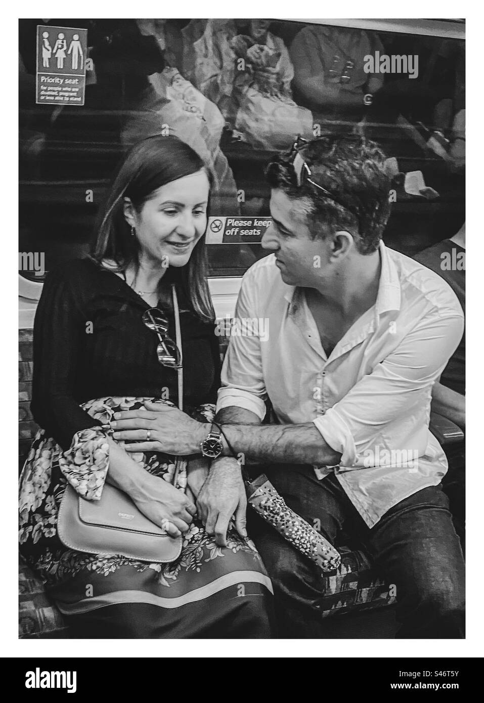 A man rests his hand on his pregnant wife’s belly on the underground in London - Smartphone Captured Stock Image