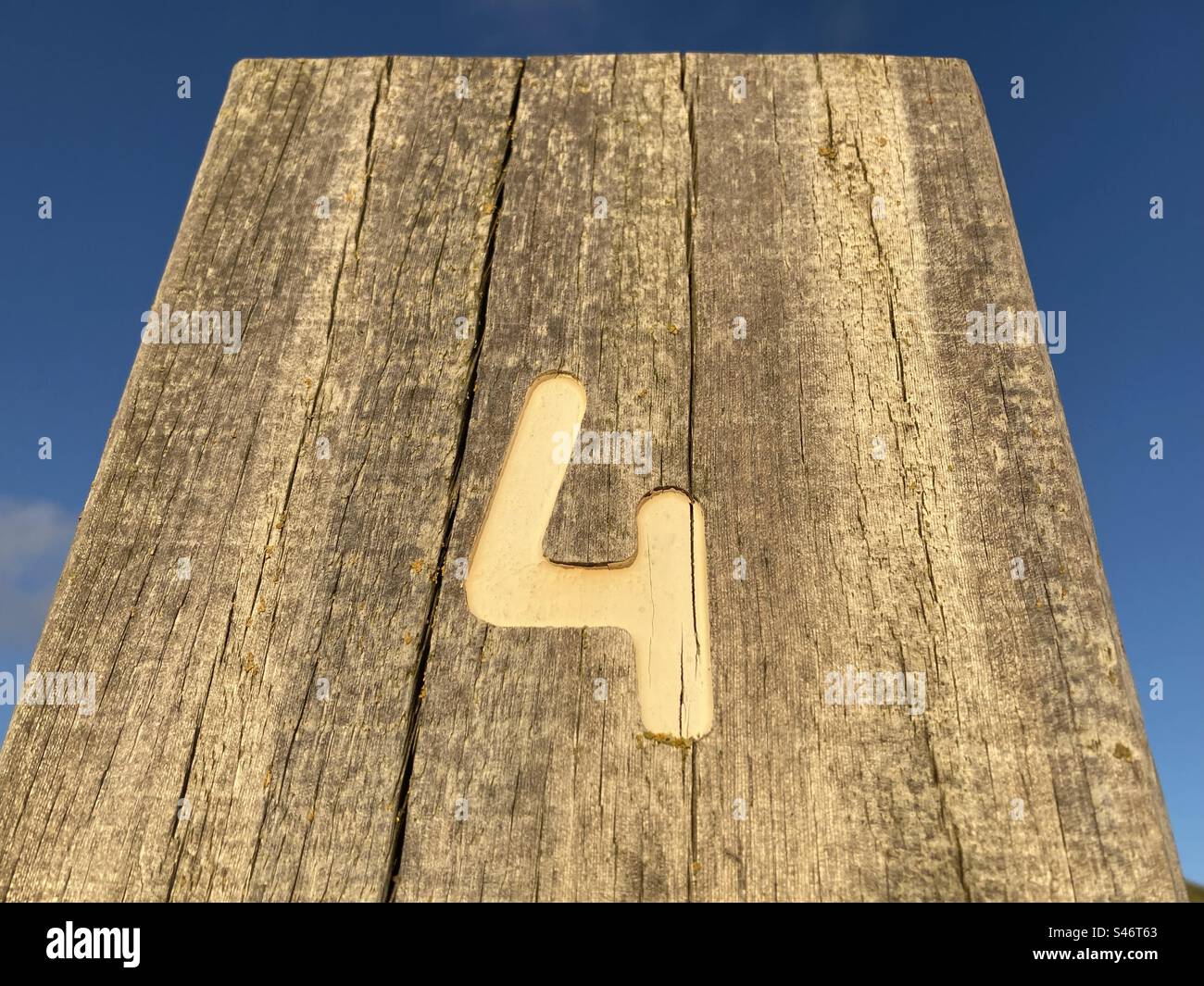 A white number four painted on a weathered wooden stake - Smartphone Captured Stock Image