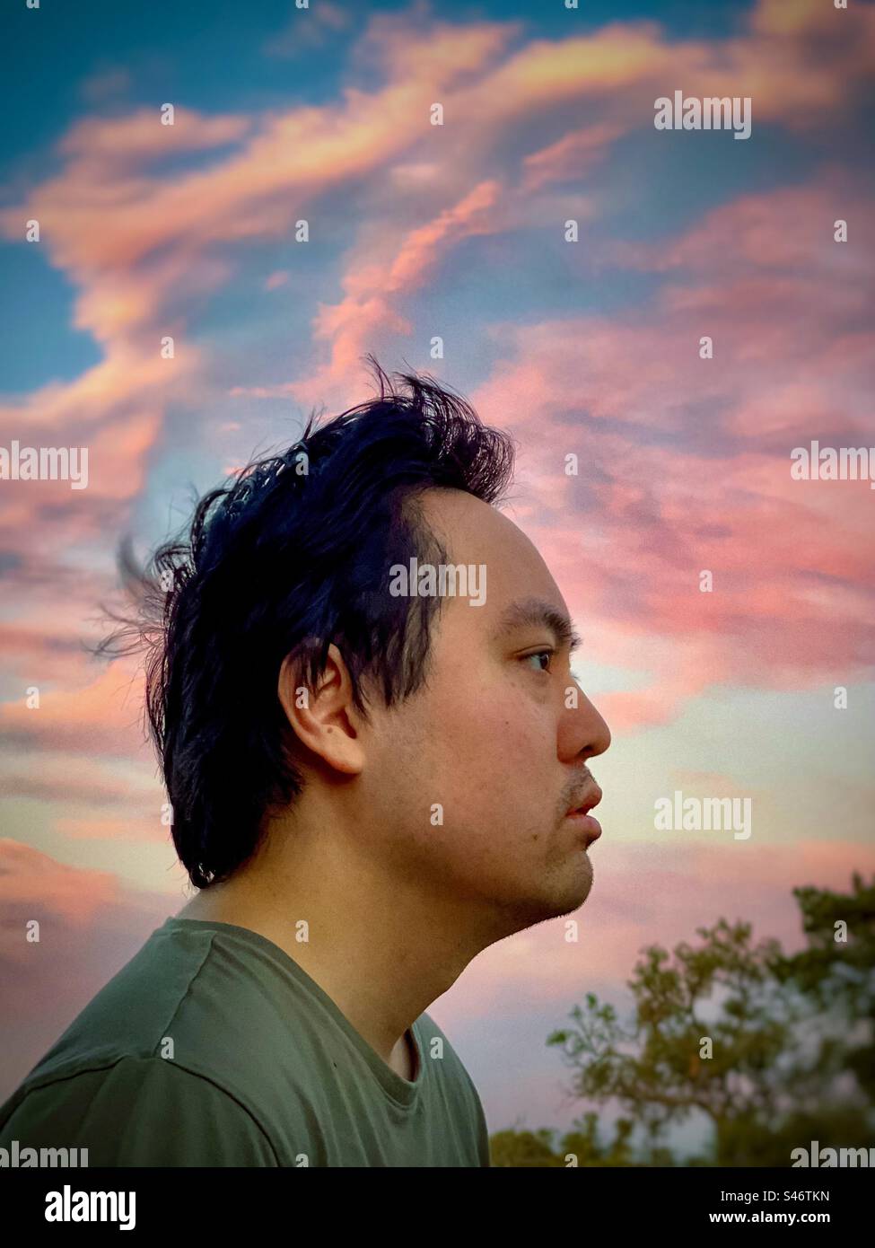 Portrait of young Asian man lost in contemplation against pink clouds in sunset sky. - Smartphone Captured Stock Image Portrait of young Asian man lost in contemplation against pink clouds in sunset sky. - Smartphone Captured Stock Image