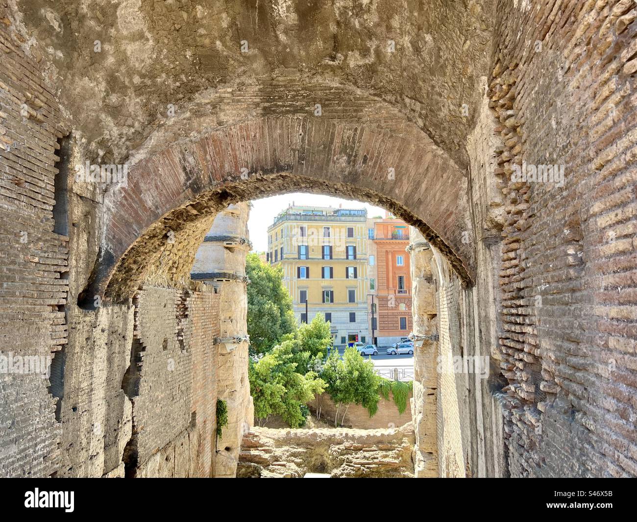 Looking out from the inside of the Roman Colosseum to colorful buildings on the street outside. Stock Photo