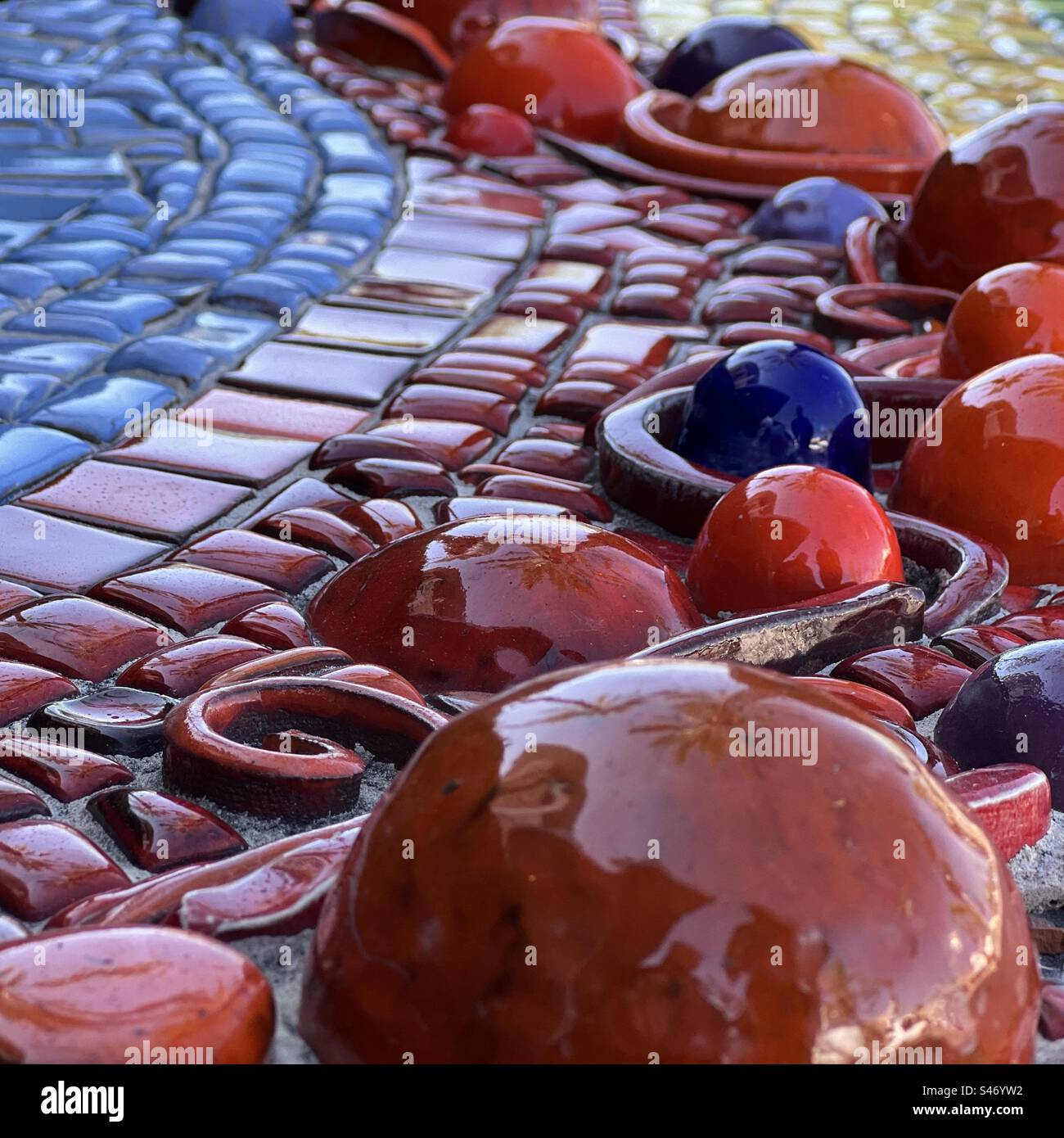 Square, closeup of blue and red ceramic shapes, with glazed red, yellow and blue tiles, part of an outdoor installation, seen in overcast light - Smartphone Captured Stock Image