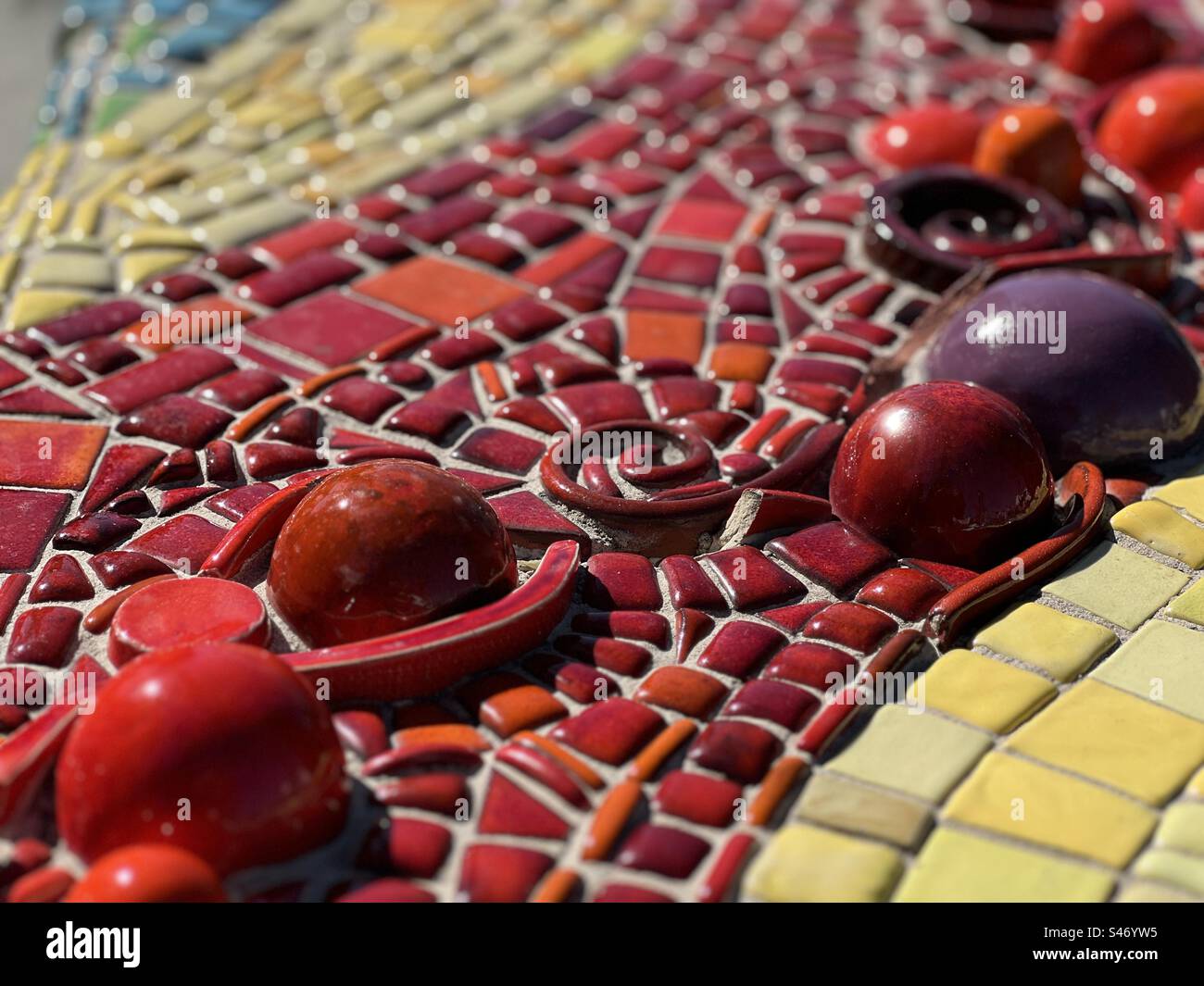 Close view of glazed red ceramic shapes, with red, yellow and blue tiles, part of an outdoor installation, seen in sunlight. Landscape format - Smartphone Captured Stock Image