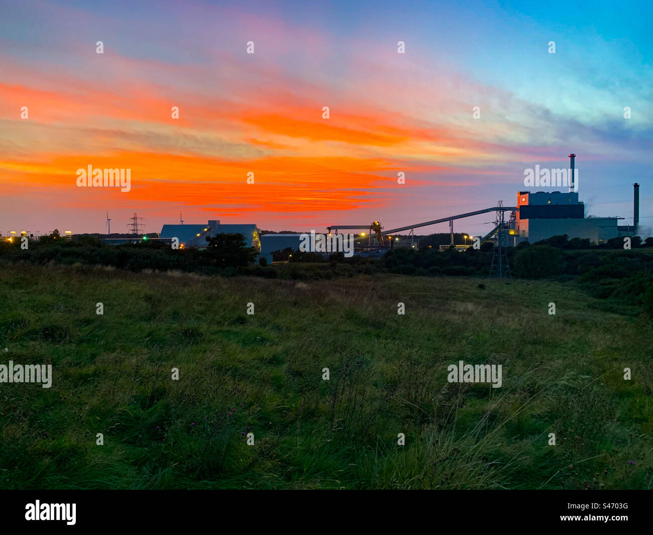 Factory with sunset in background and green field in foreground