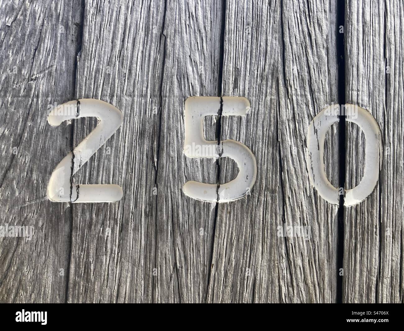 A white number 250 painted on a weathered wooden stake - Smartphone Captured Stock Image
