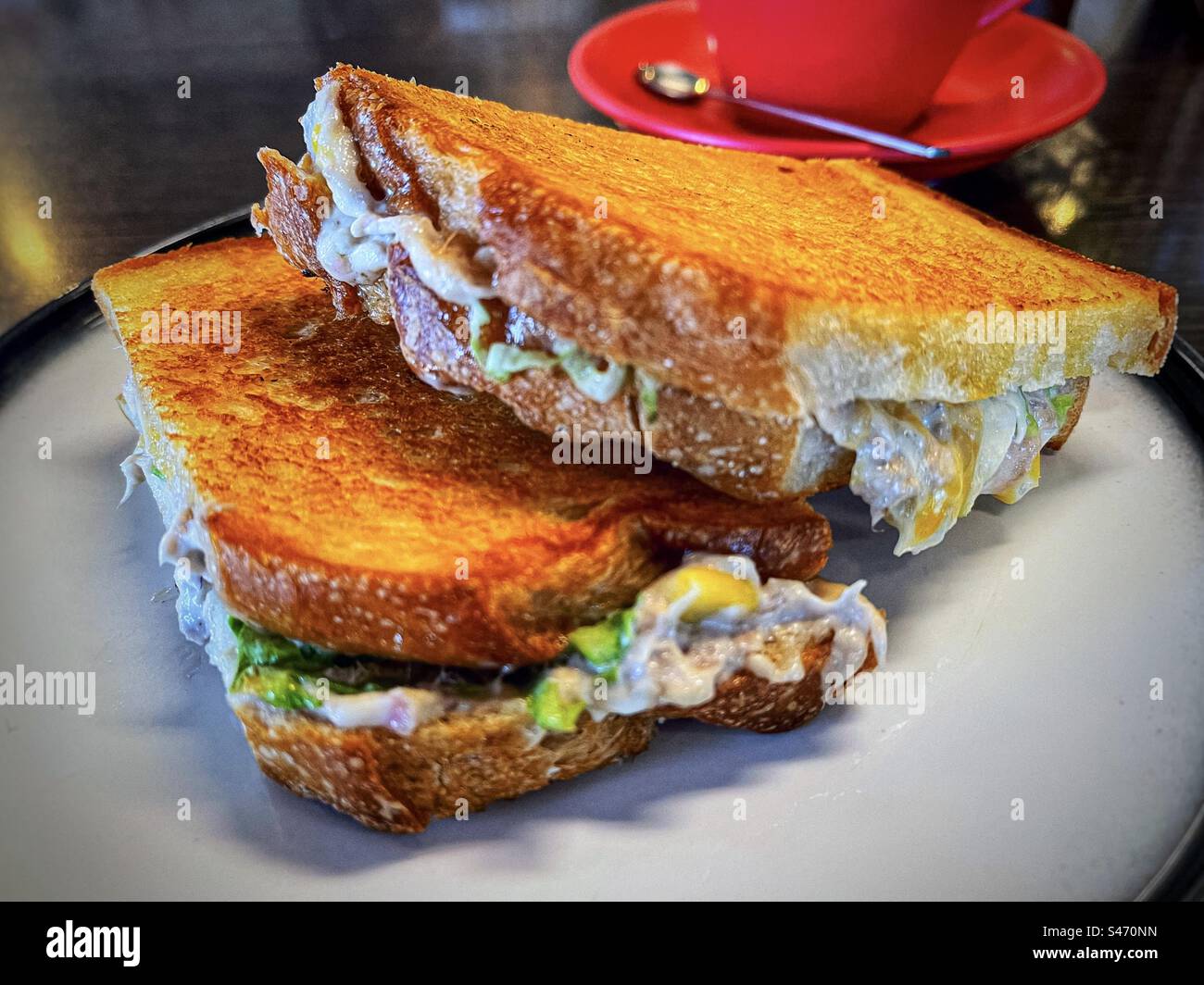 Close-up of tuna cheese toasties on plate on table with red coffee cup and saucer. - Smartphone Captured Stock Image