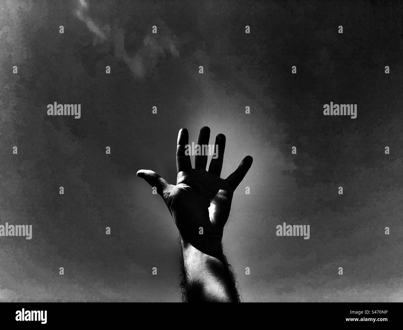 Dramatic  black and white image of a raised hand against the sky Stock Photo