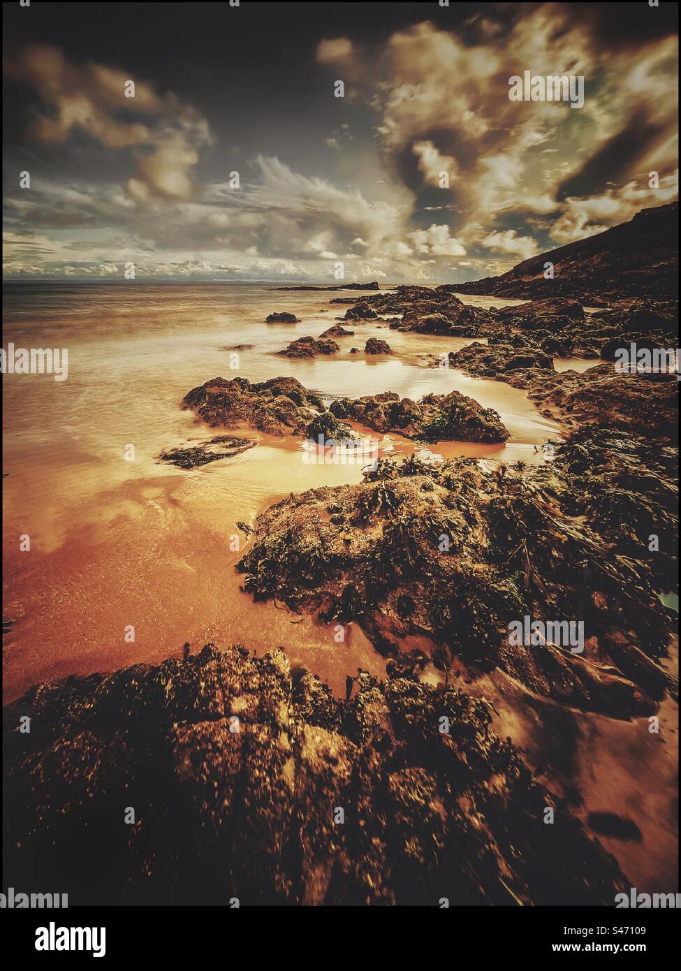 Rocks on a Sandy beach with clouds in a blue sky - Smartphone Captured Stock Image