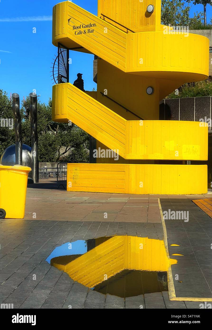 Yellow spiral staircase, yellow wheelie bin and reflection in puddle. Festival Hall on London South Bank Stock Photo