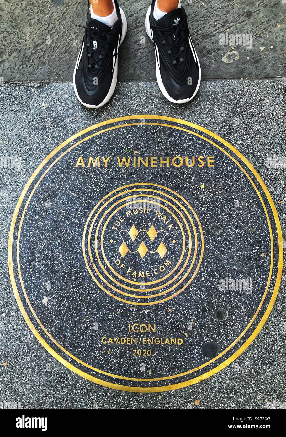 Tourist in black and white shoes looking at the Amy Winehouse music walk of fame plaque in Camden, London - Smartphone Captured Stock Image
