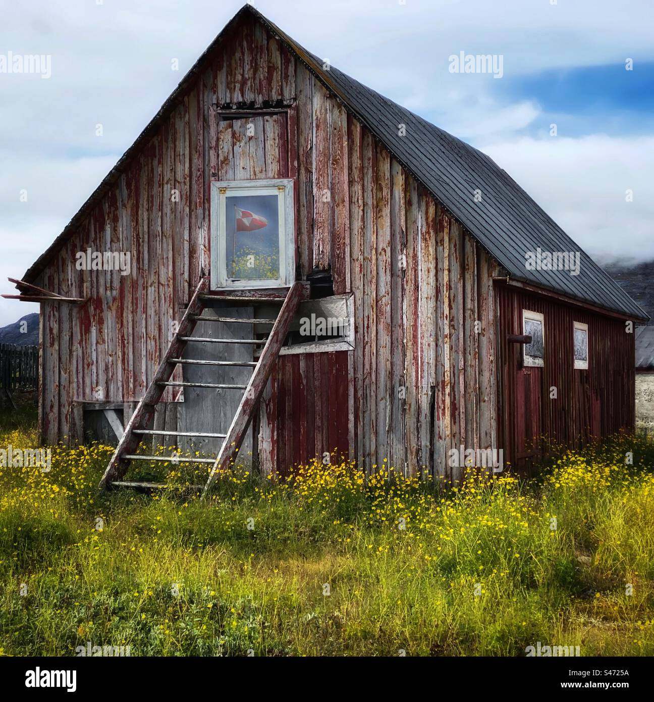 An abandoned barn in Greenland with the national flag reflected in the window - Smartphone Captured Stock Image
