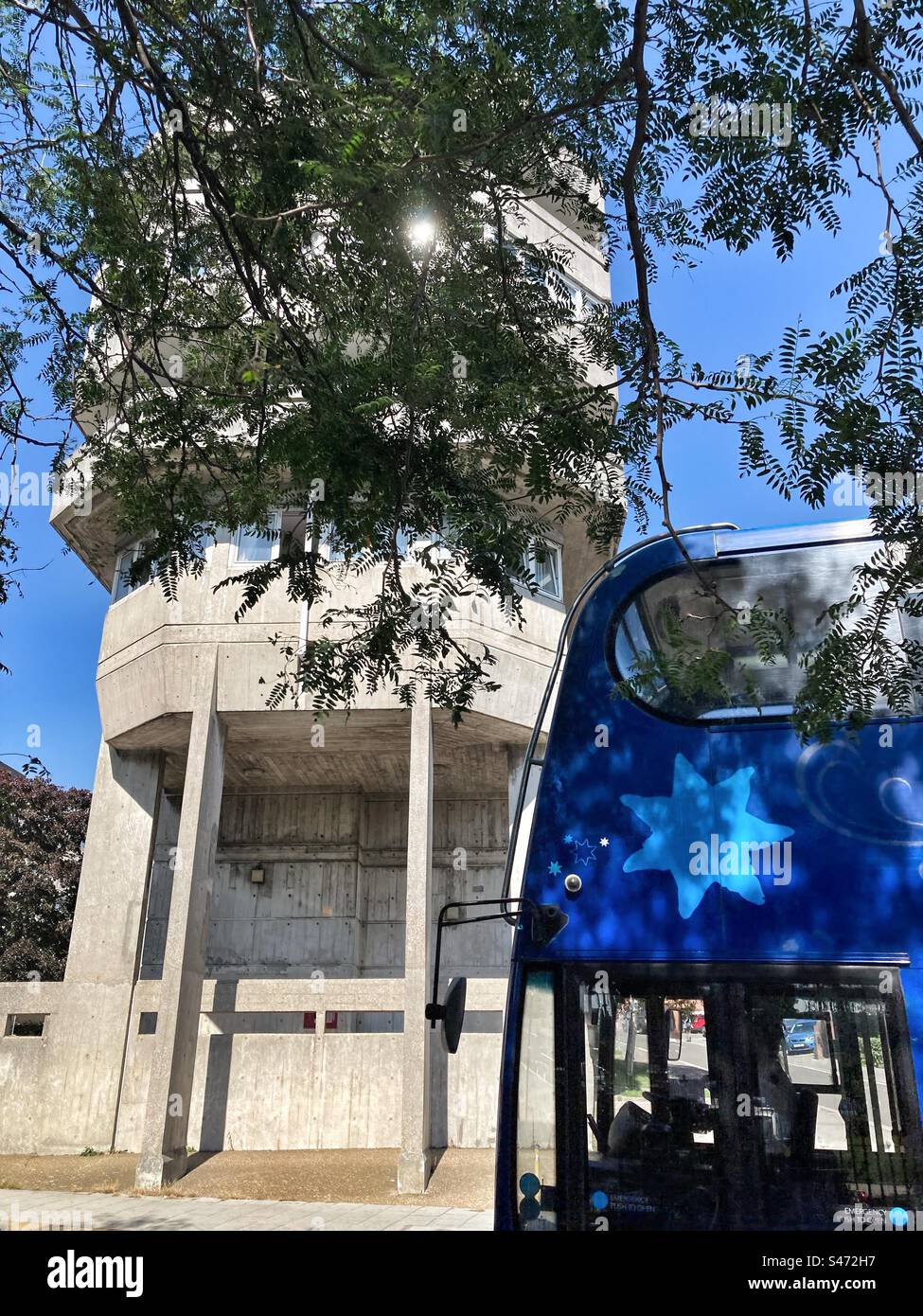 Blue line bus passing and concrete building with tree branches in close up view, in Southampton,Hampshire,UK - Smartphone Captured Stock Image