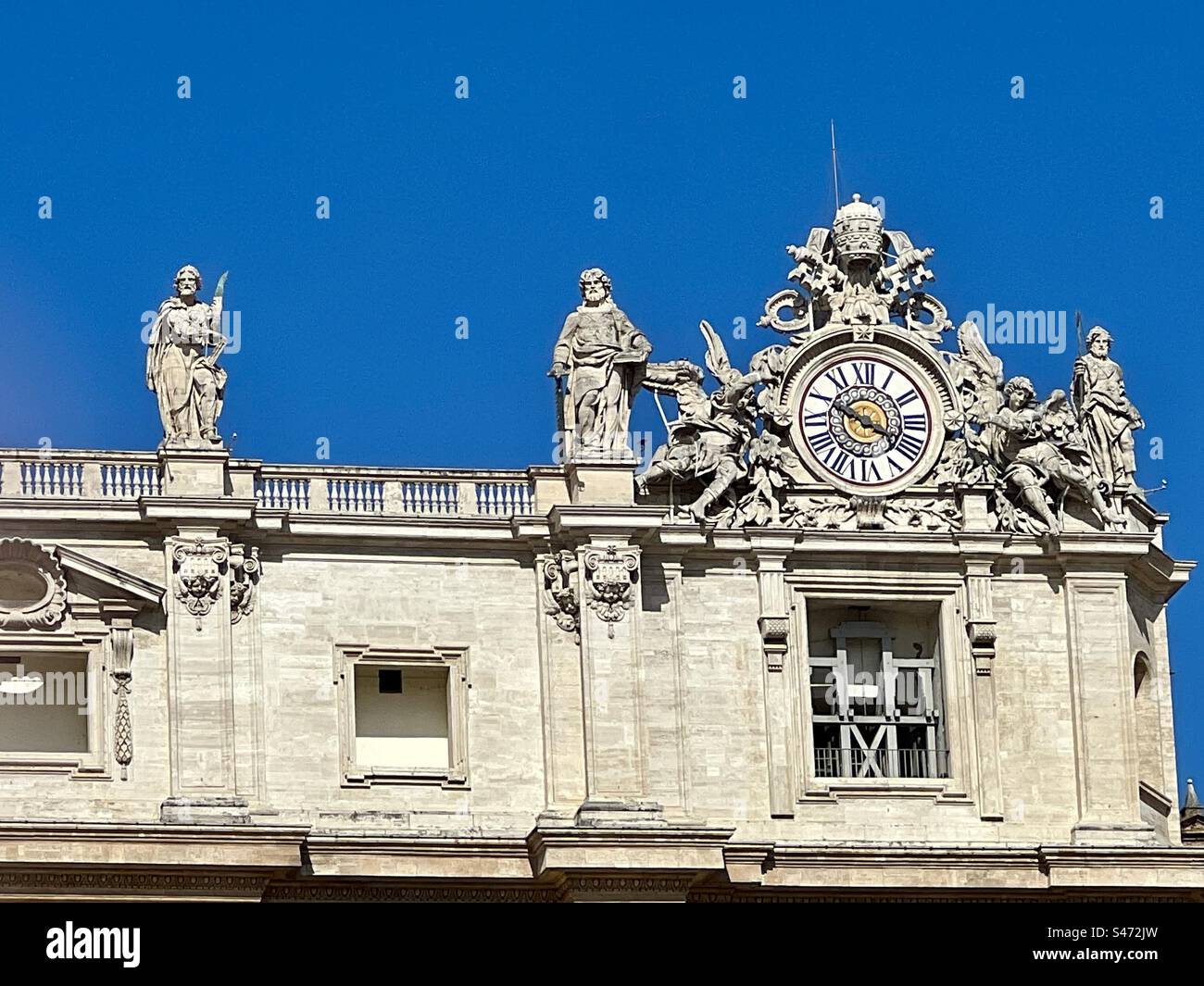 The ornate clock on the top right of Saint Peter’s Basilica along with statues of saints, Vatican City. - Smartphone Captured Stock Image