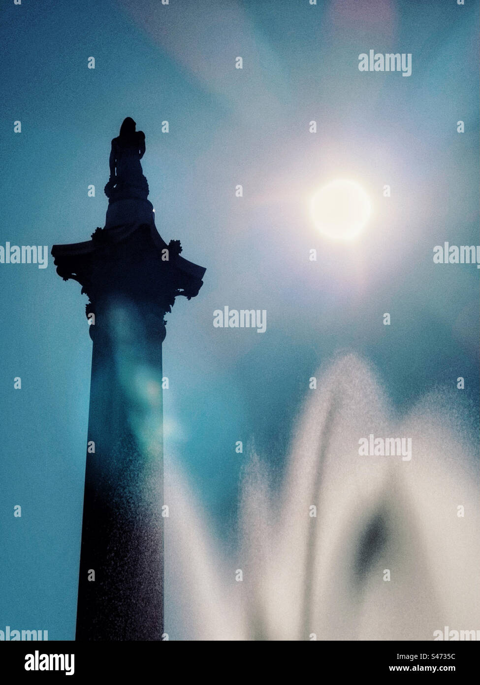 Moody image of Nelson’s Column against bright sun with blurred fountain in foreground Stock Photo