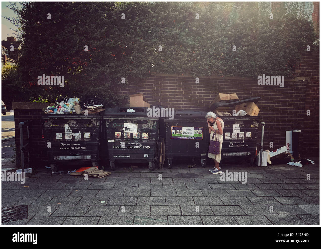 Elderly woman on mobile standing by industrial waste bins - Smartphone Captured Stock Image