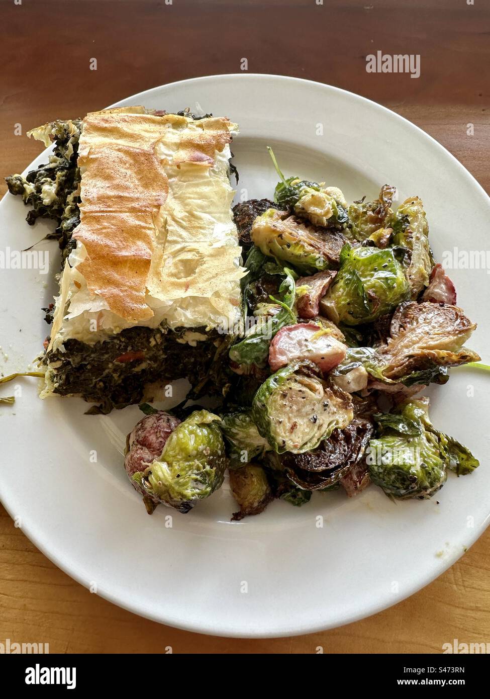 Spinach pie with roasted brussels sprouts on a white plate. Wooden table as background. - Smartphone Captured Stock Image