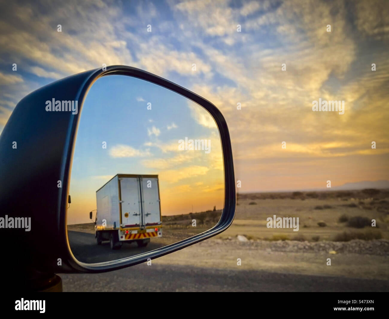 A truck passes a car seen in the wing mirror of a car on the road in Namibia - Smartphone Captured Stock Image