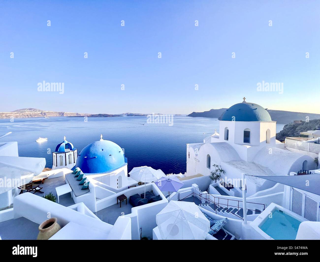 The White Churches With Blue Domes Nestled On The Slopes Of The Caldera the-white-churches-with-blue-domes-nestled-on-the-slopes-of-the-caldera