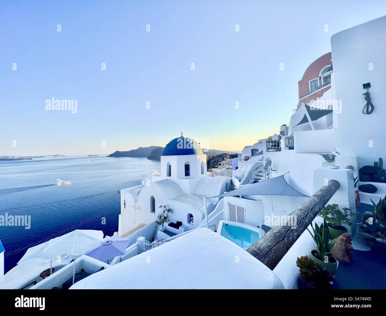 The blue dome of Anastasi church stands out amongst the white buildings and the Aegean Sea as sun begins to set. Santorini, Greece - Smartphone Captured Stock Image
