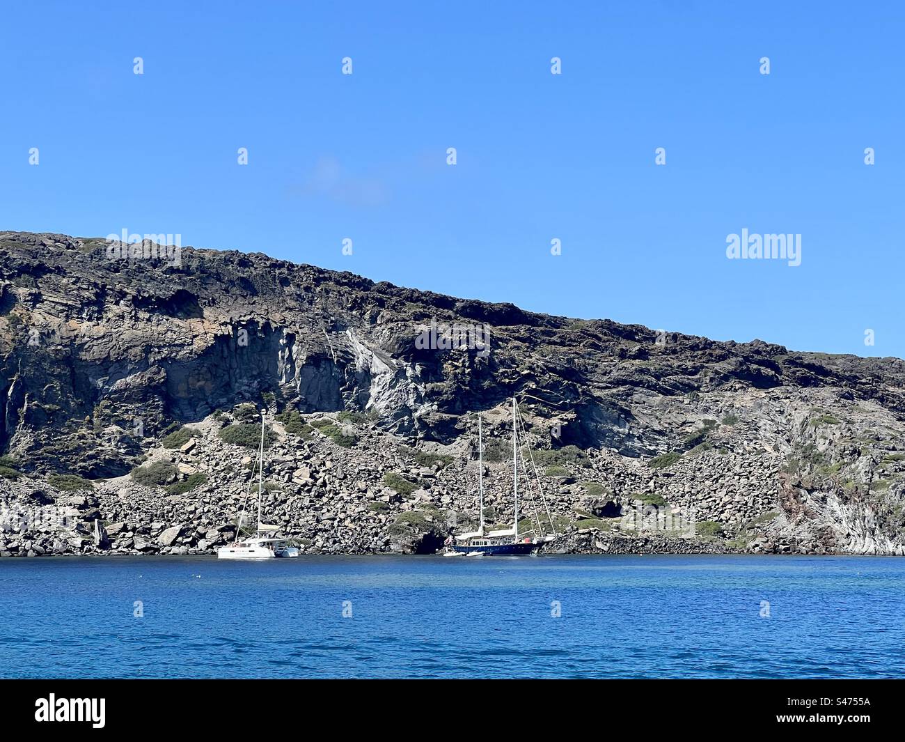 Nea Kameni island coastline with boats in the Aegean Sea, near Santorini island. - Smartphone Captured Stock Image