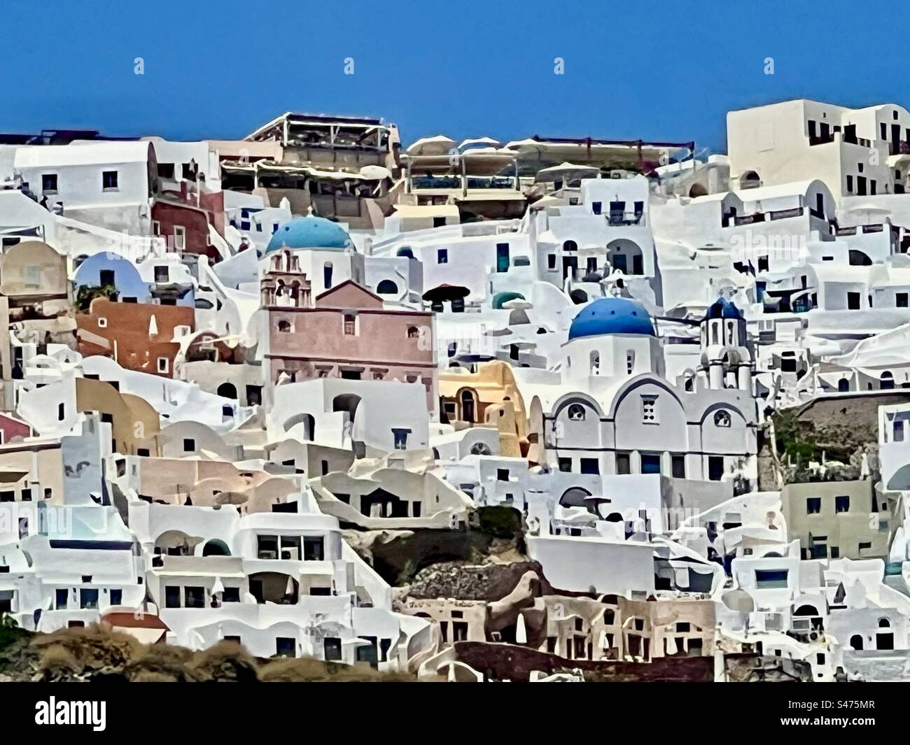 Colorful blue church domes and structures amid many white buildings that sit above the Santorini island caldera in Oia. Stock Photo