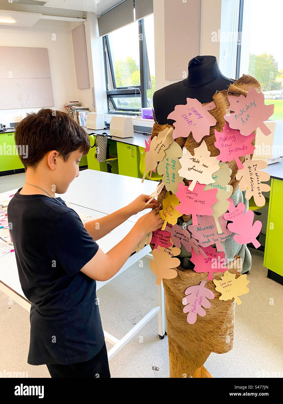 A boy pins a paper leaf shape with a sentiment written on it onto a dress made up of sentiments at a school open evening. - Smartphone Captured Stock Image