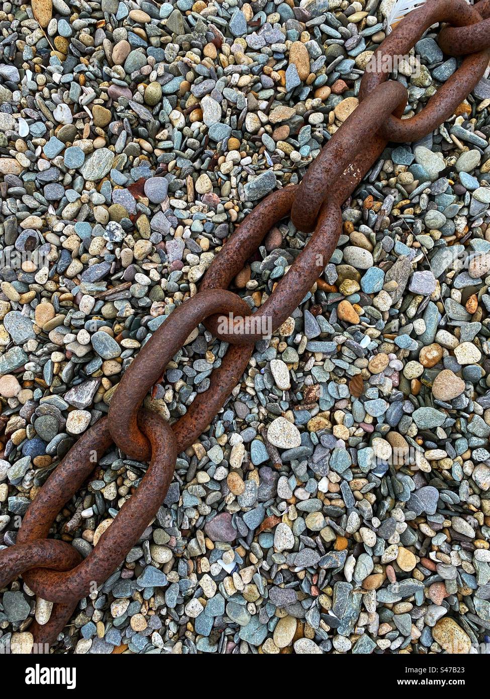 A large rusty chain lying on shingle beach - Smartphone Captured Stock Image
