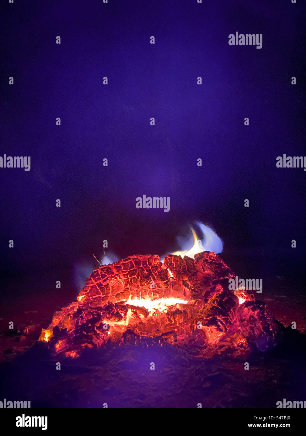 The burning embers of a campfire with blue smoke all around - Smartphone Captured Stock Image