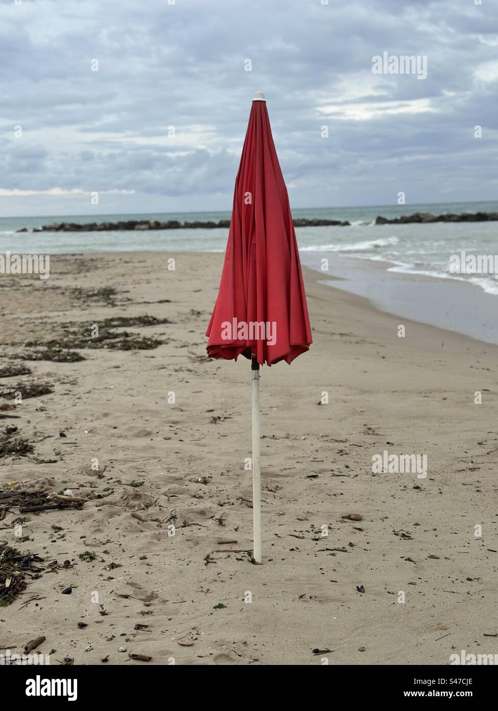 Red closed umbrella on the beach front of the sea, summer season end conceptual photo - Smartphone Captured Stock Image