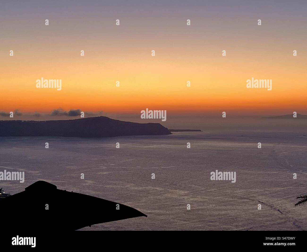 Orange sky as the sun sets into the horizon, overlooking Thirasia island from Fira on Santorini. - Smartphone Captured Stock Image