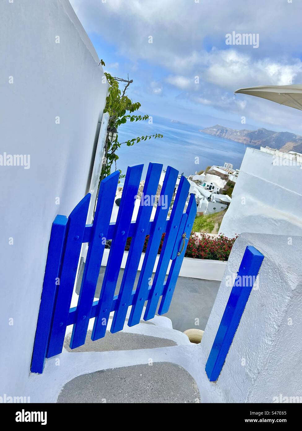 A vibrant blue gate in Oia leads down a path with the caldera in the Aegean Sea below Santorini - Smartphone Captured Stock Image