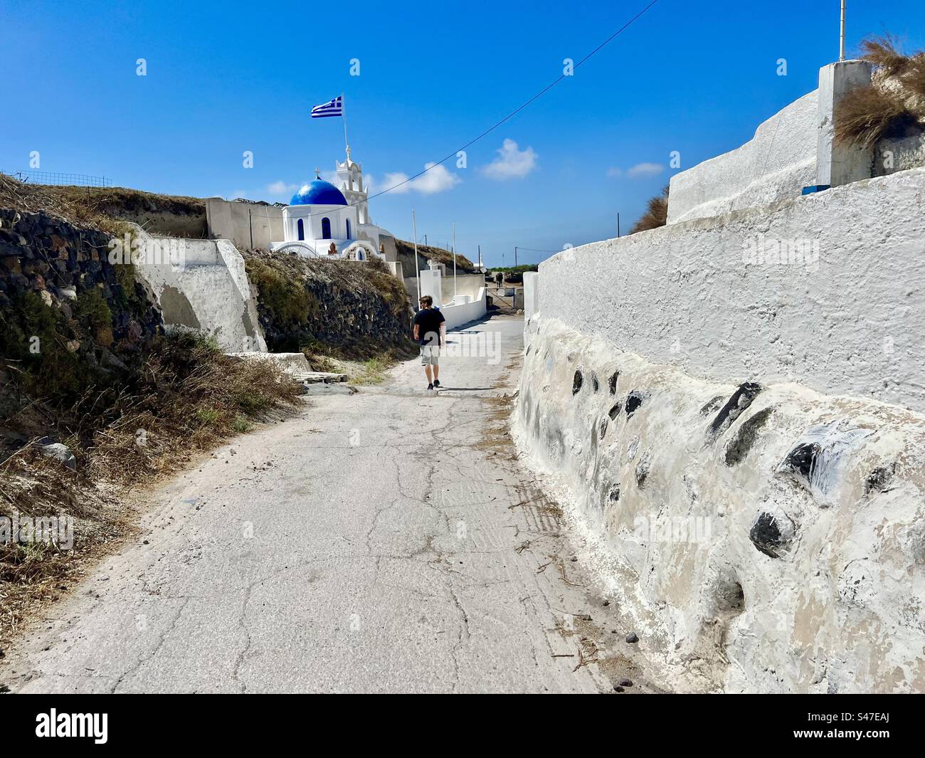 Young man exploring a street in Megalochori where the blue dome church of Saint Paraskevi is located. - Smartphone Captured Stock Image