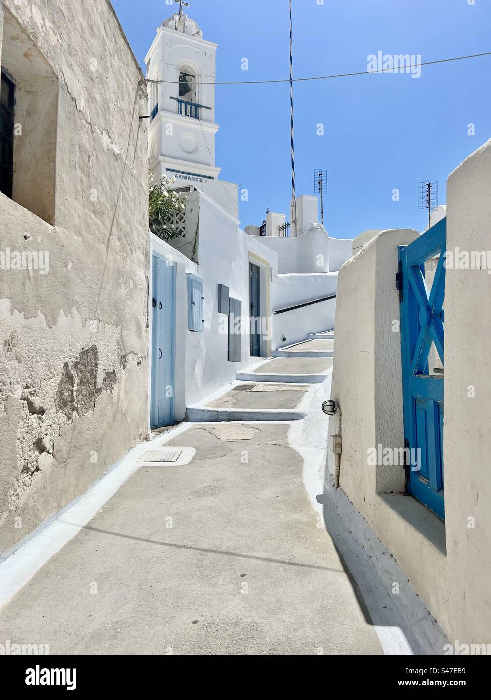 Beautiful, inclined street of Megalochori village lined with the traditional white washed buildings and painted blue accents on entryways. Stock Photo