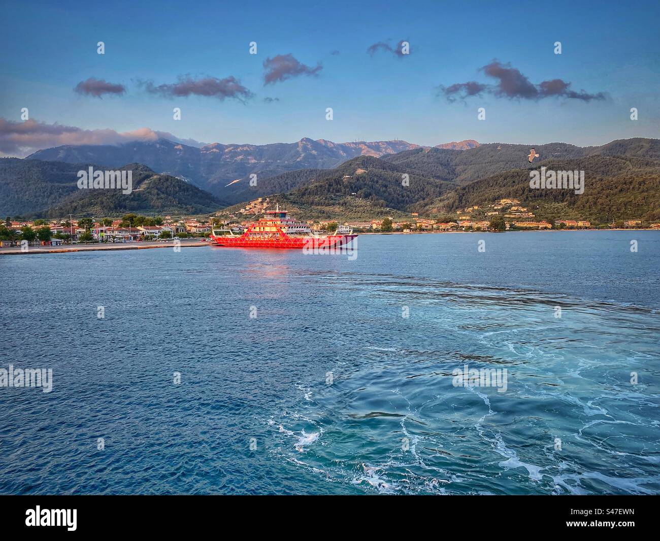 Early morning view at blue sea, red ferry boat and mountains in Limenas harbor on Thassos island, Greece. - Smartphone Captured Stock Image