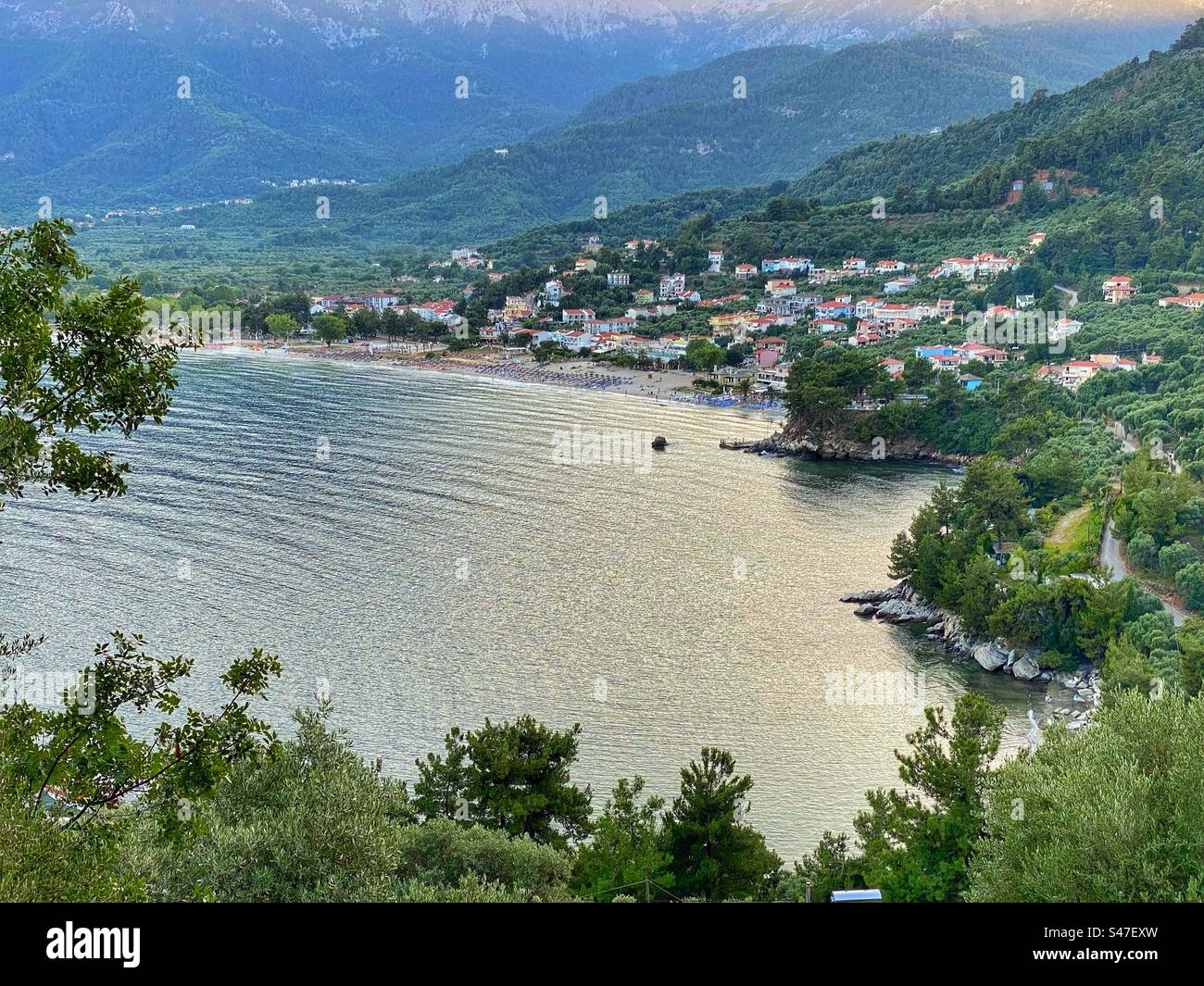 Sunset high-angle sea view at Golden Beach town surrounded by green forests and trees on Thassos island, Greece. - Smartphone Captured Stock Image