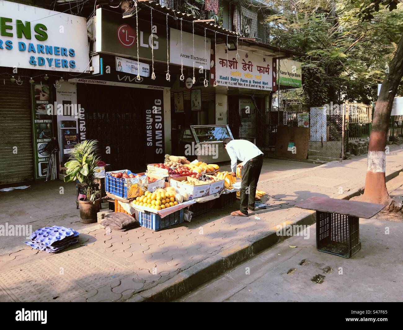 A fruit vendor on a pavement in Mumbai, India with shops in the background - Smartphone Captured Stock Image