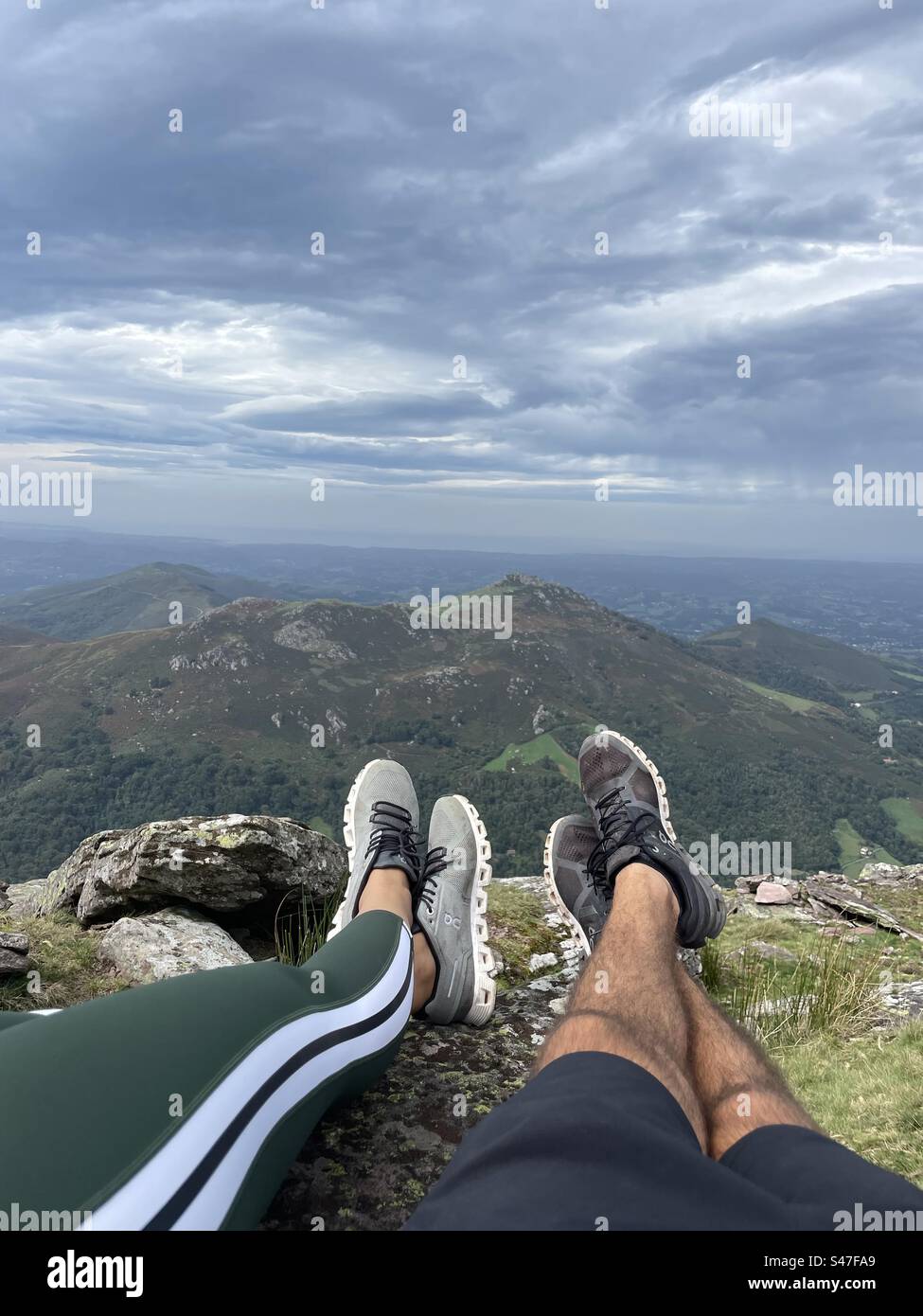 Legs of a couple laying down at the top of a mountain with a view. Stock Photo