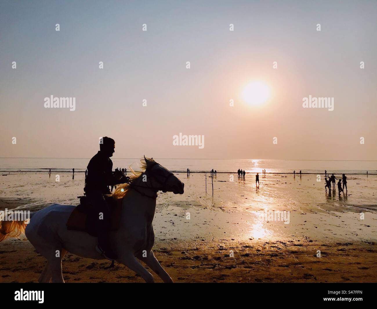 A man riding a horse on the beach during sunset Stock Photo