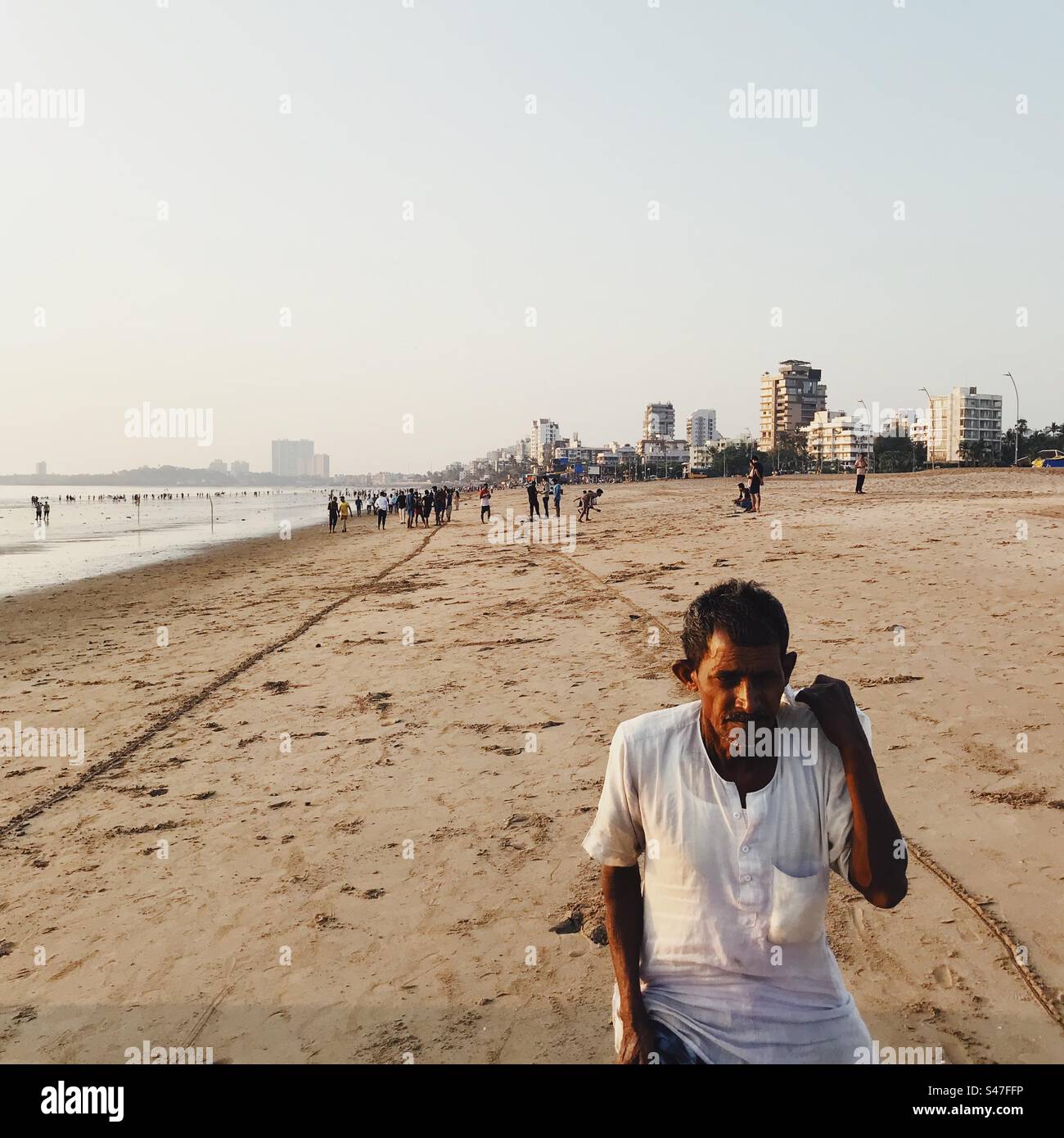 An elderly Indian man walking on the beach in Mumbai, India with skyscrapers in the background - Smartphone Captured Stock Image