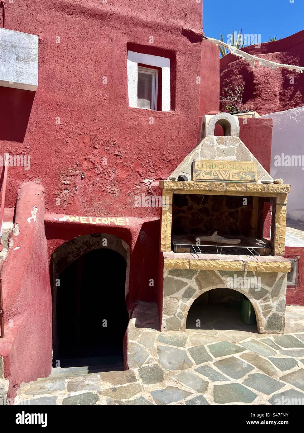On a side street in Megalochori village on Santorini is a unique red building with an entrance to unground caves. Sign over the cave entrance welcomes people to go inside. - Smartphone Captured Stock Image