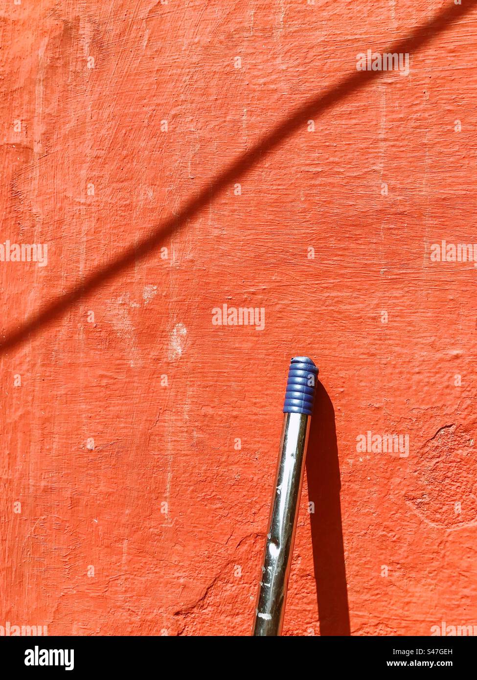 A portion of a mop resting against a red wall - Smartphone Captured Stock Image