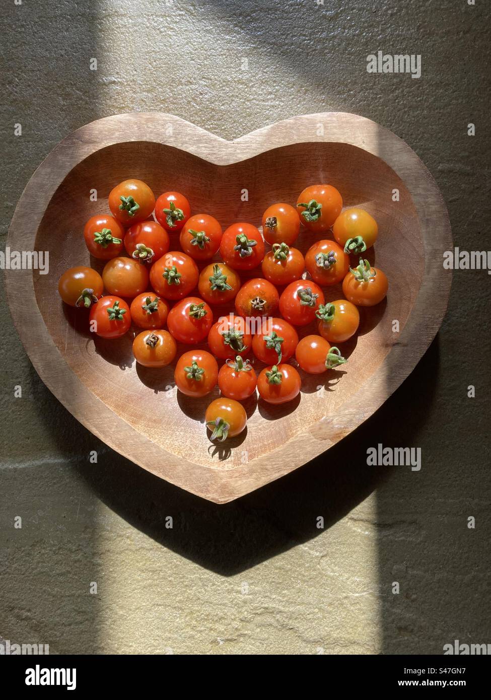 Heart shaped wooden bowl with home grown cherry tomatoes in a shaft of sunlight Stock Photo